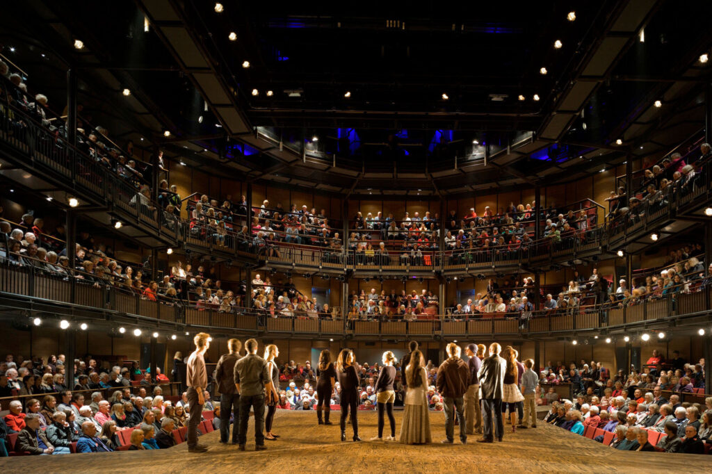 Performers stand on a stage that juts into the audience.