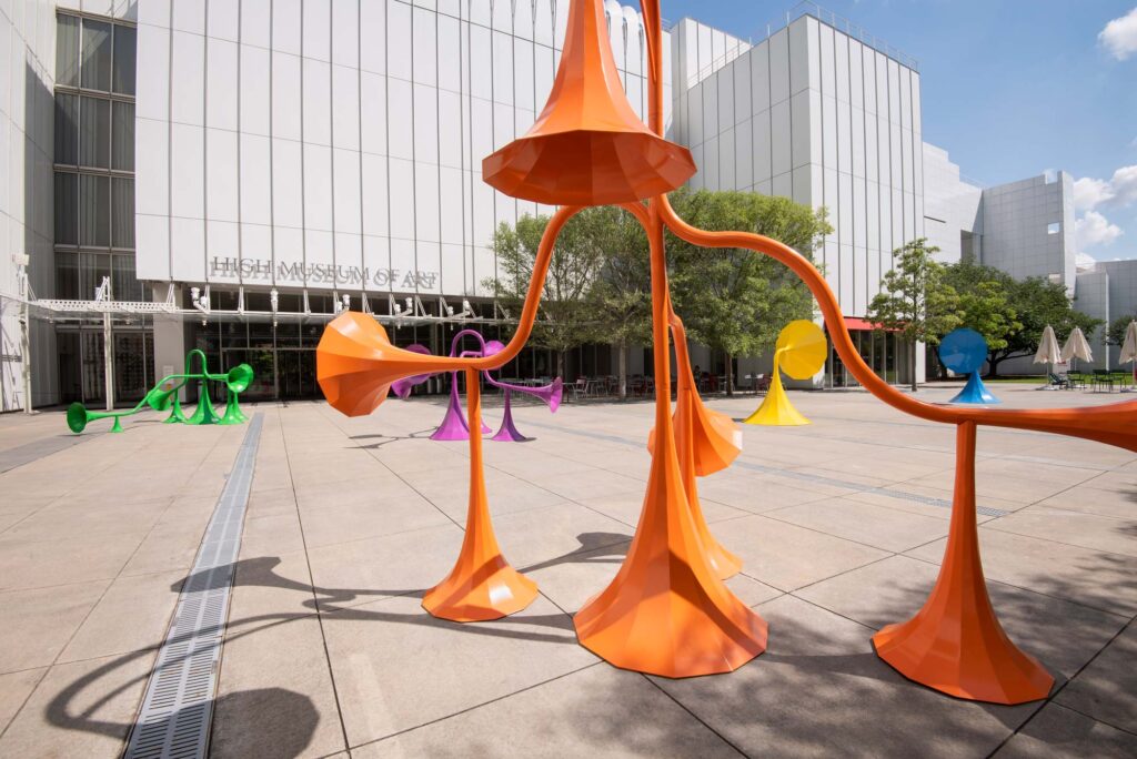 A close up of an orange sound sculpture. The other sculptures appear in the background in the plaza of High Musuem of Art.