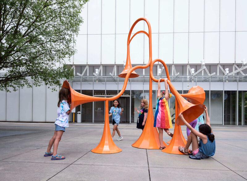 Kids playing with large orange sound sculpture.