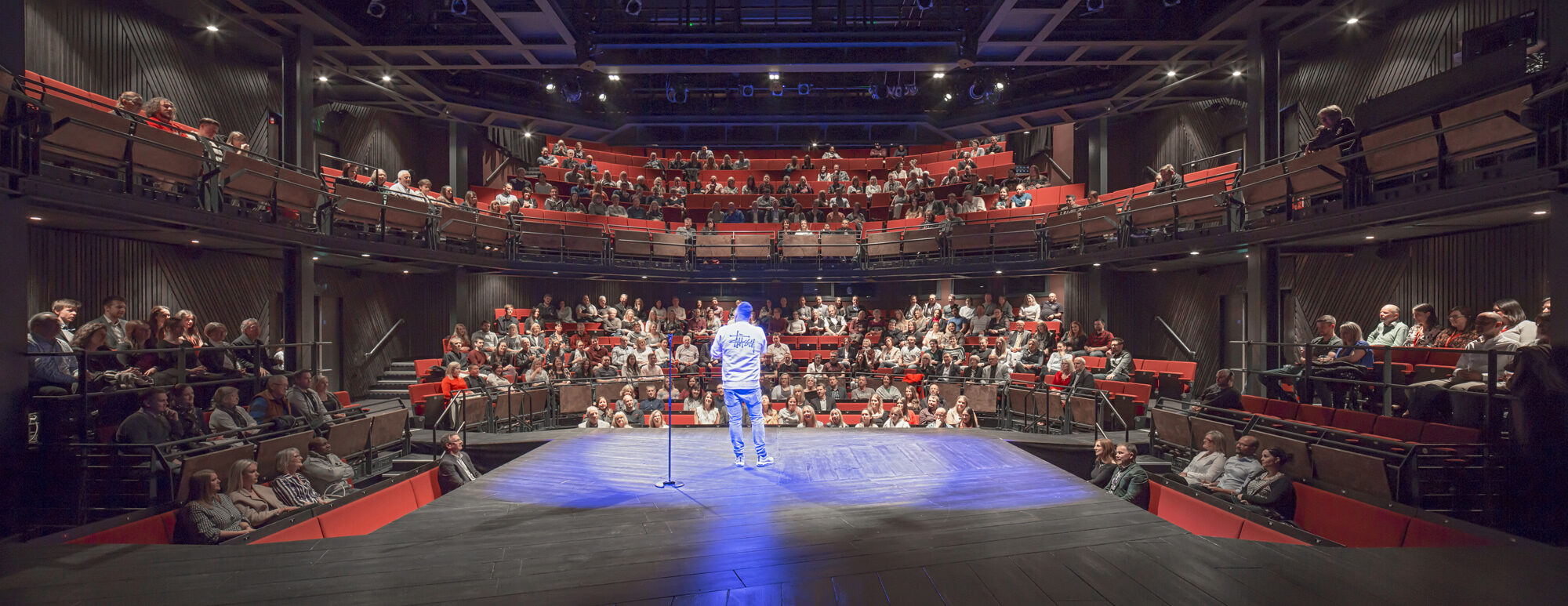 A performer on stage interacts with an audience. Photo by Peter Cook.