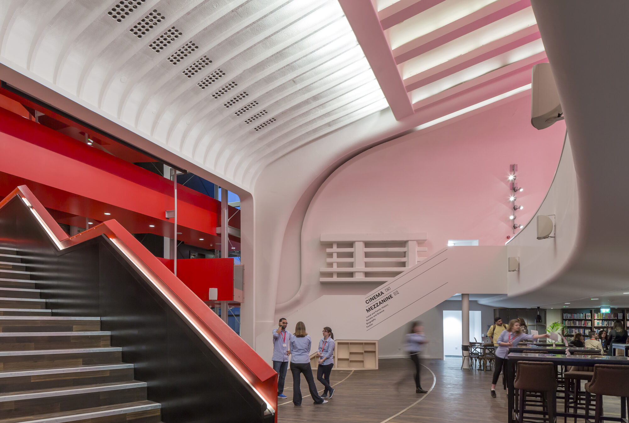 A transitional space with sloping white ceiling and two red and white stairwells leading up. Photo by Peter Cook.
