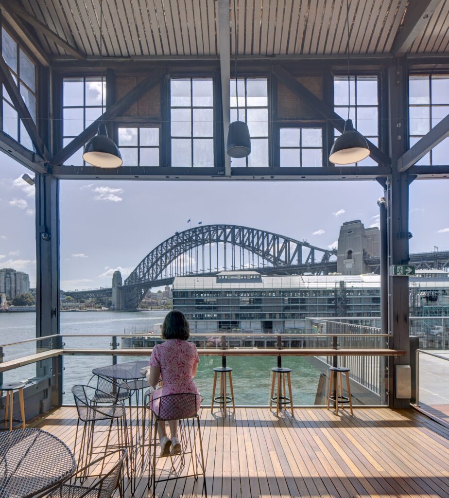 A woman looks out at Sydney Harbour Bridge from a cafe seating area.