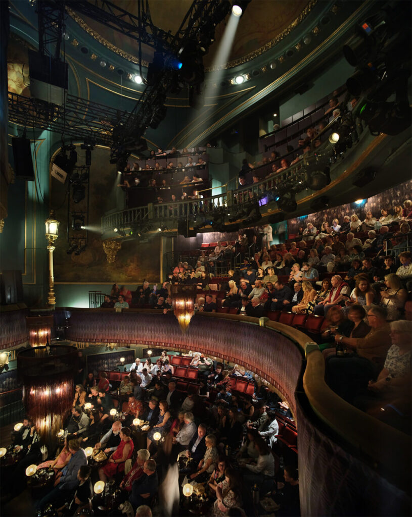 The audience looks on from the three levels of seating.