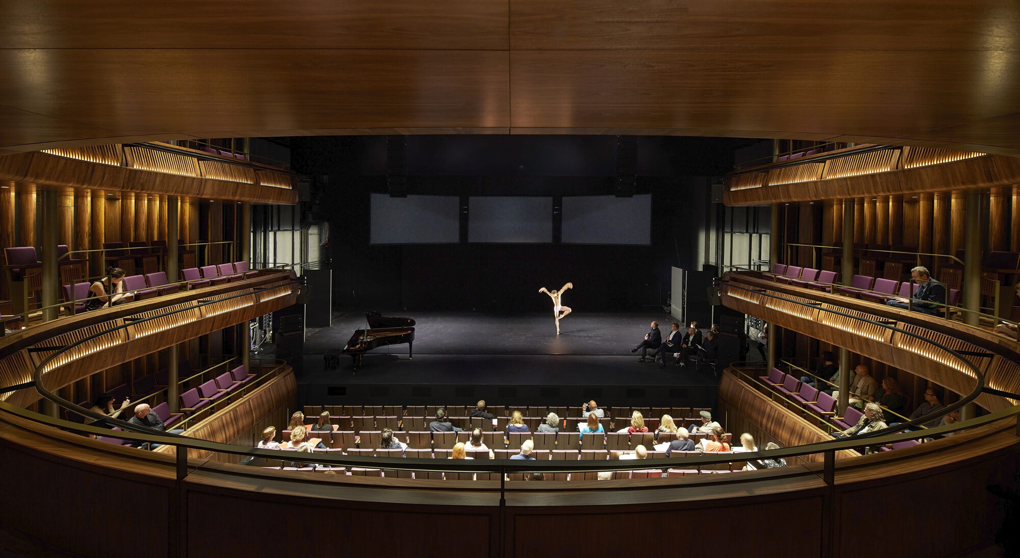 A dancer practices on stage as people look on.