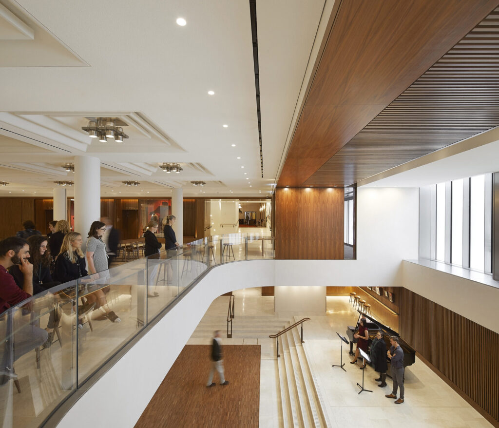 People look down from the cafe seating area toward the performers by the piano on the level below.