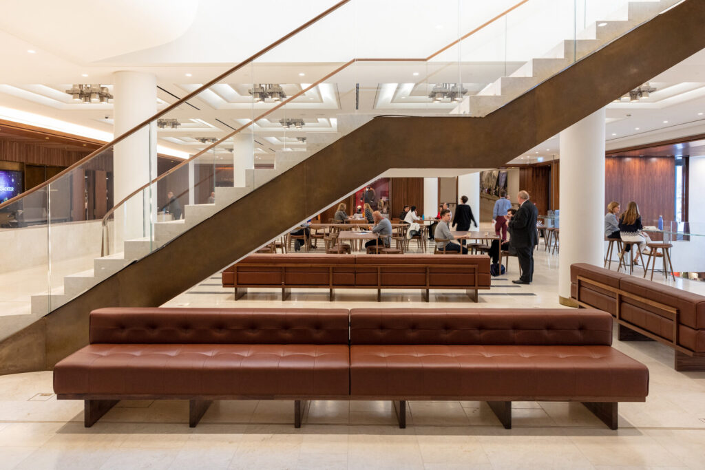 A bronze stairwell leading up from café area. Brown padded benches frame the area beneath the stairwell.