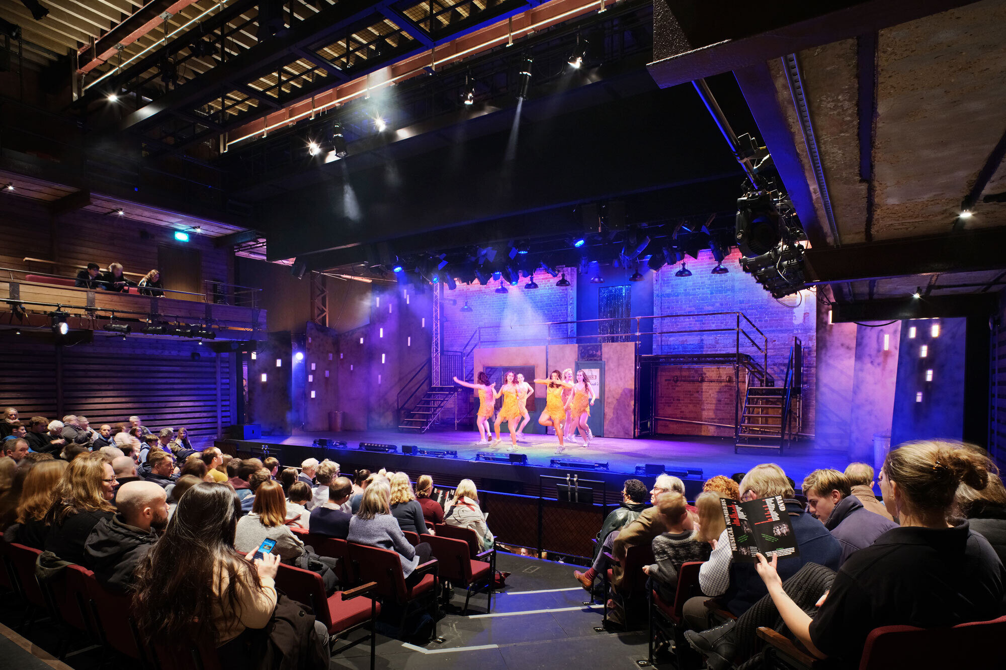 Families watch a performance of several girls in yellow dresses on stage.