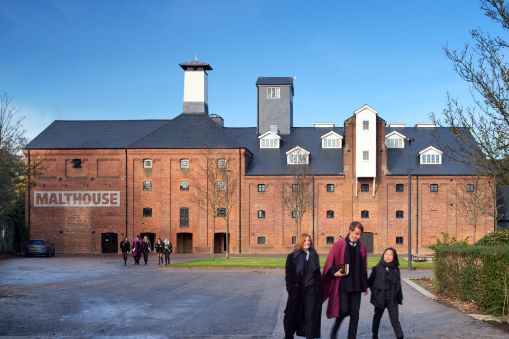 A brick building with several dormer windows and tower structures rising from the from roof. "Malthouse" is painted in white on the left end of the building.