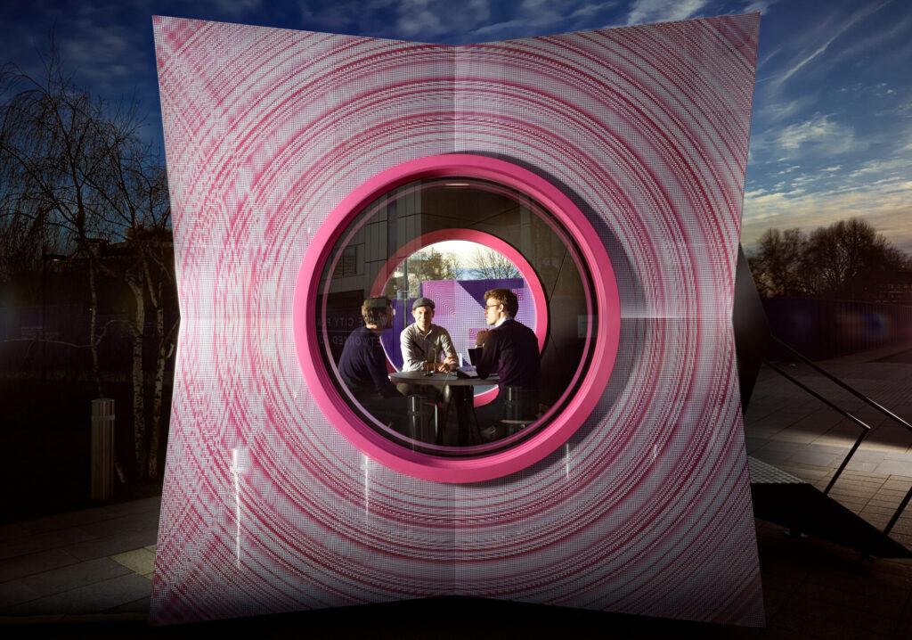 Three men sitting in the Pod at night, seen through its circular window.