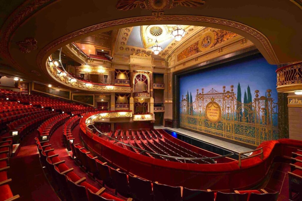 View of the stage from the first balcony. A decorative screen across the stage area has a painting of an elaborate gate that says "For Thine Especial Safety".