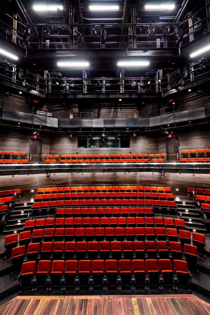 The red seating and balcony level seen from stage. Above are layers of catwalk with technical equipment.