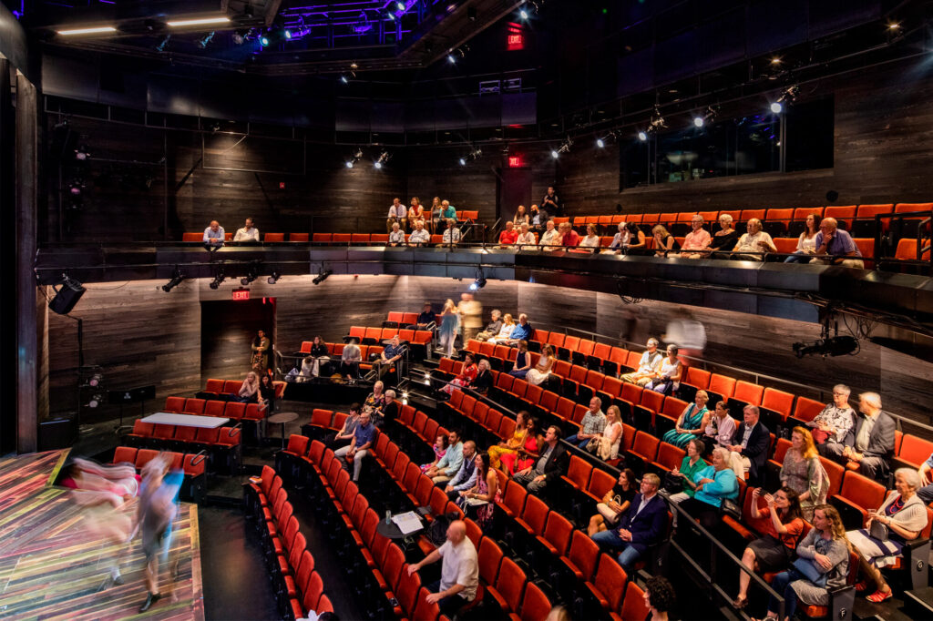Long exposure view of a scattered audience watching movement on stage.