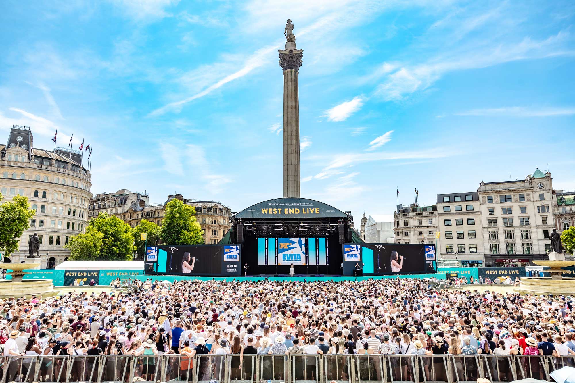 A crowd outside watches a performance on a stage beside Nelson's Column in Trafalgar Square.