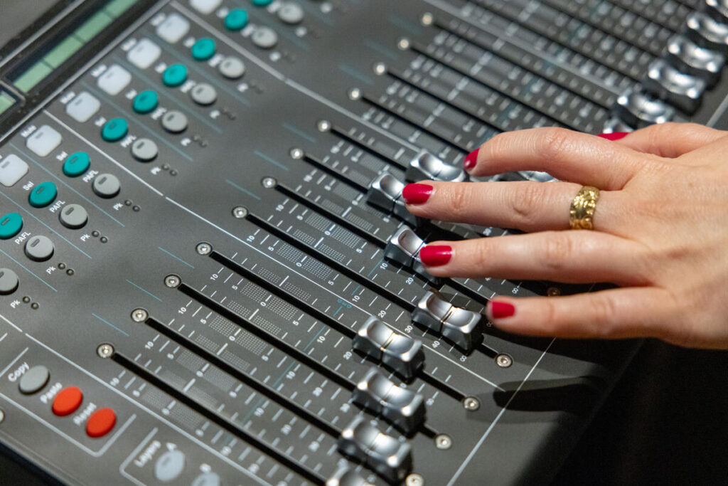 A person adjusts the levels on a soundboard.